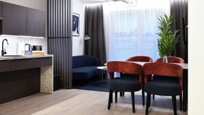 A modern hotel room with a kitchen area, a dining table with chairs, a sofa, and a large window with curtains. - BRIGHT Schloß Holte-Stukenbrock (Schloss Holte-Stukenbrock)