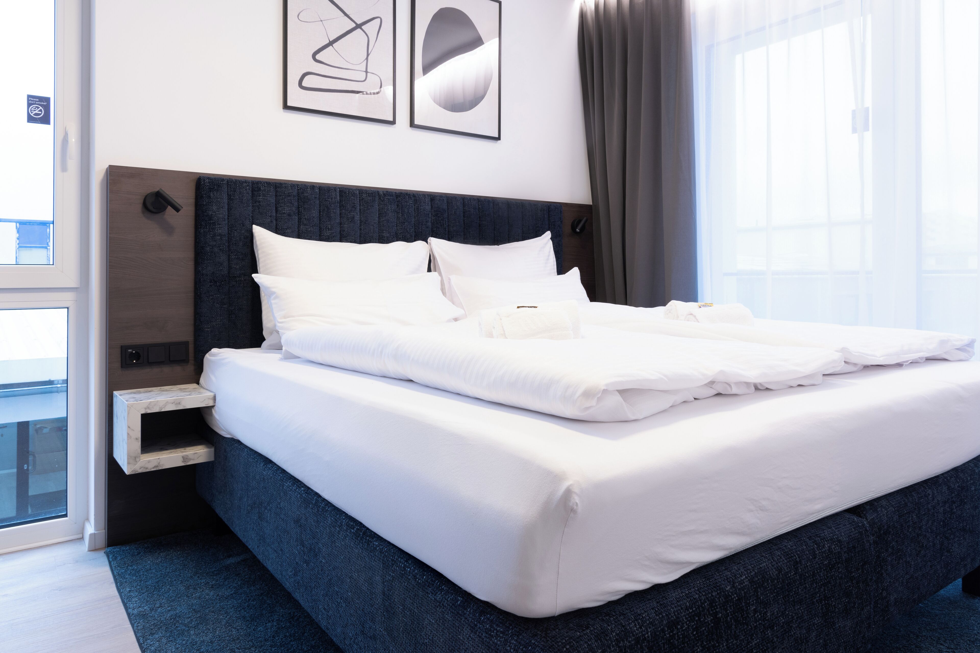 A modern hotel room with a large bed, a bedside table, and a window with curtains.