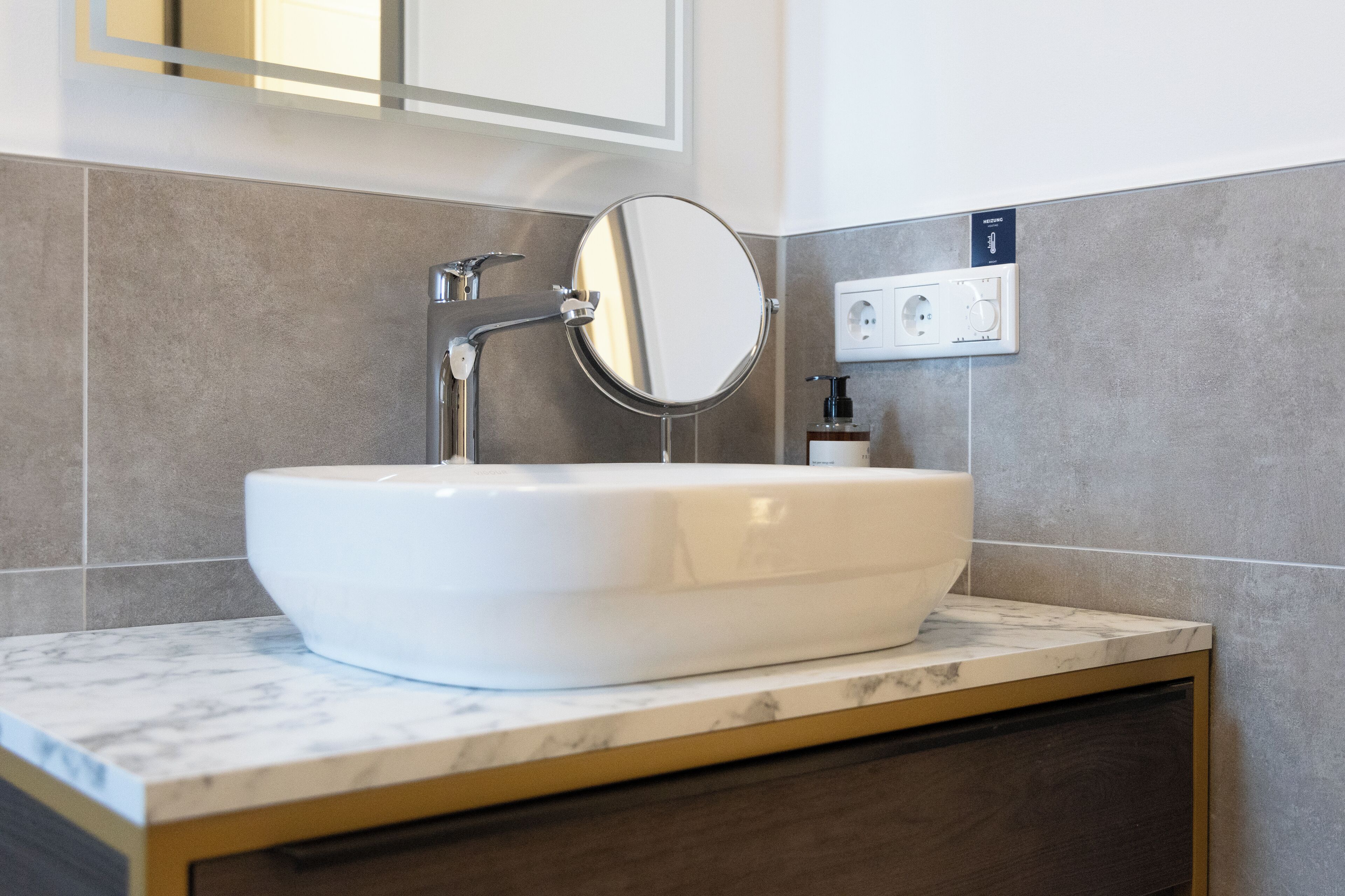 A bathroom with a white sink, a mirror, and a wall-mounted electrical outlet.