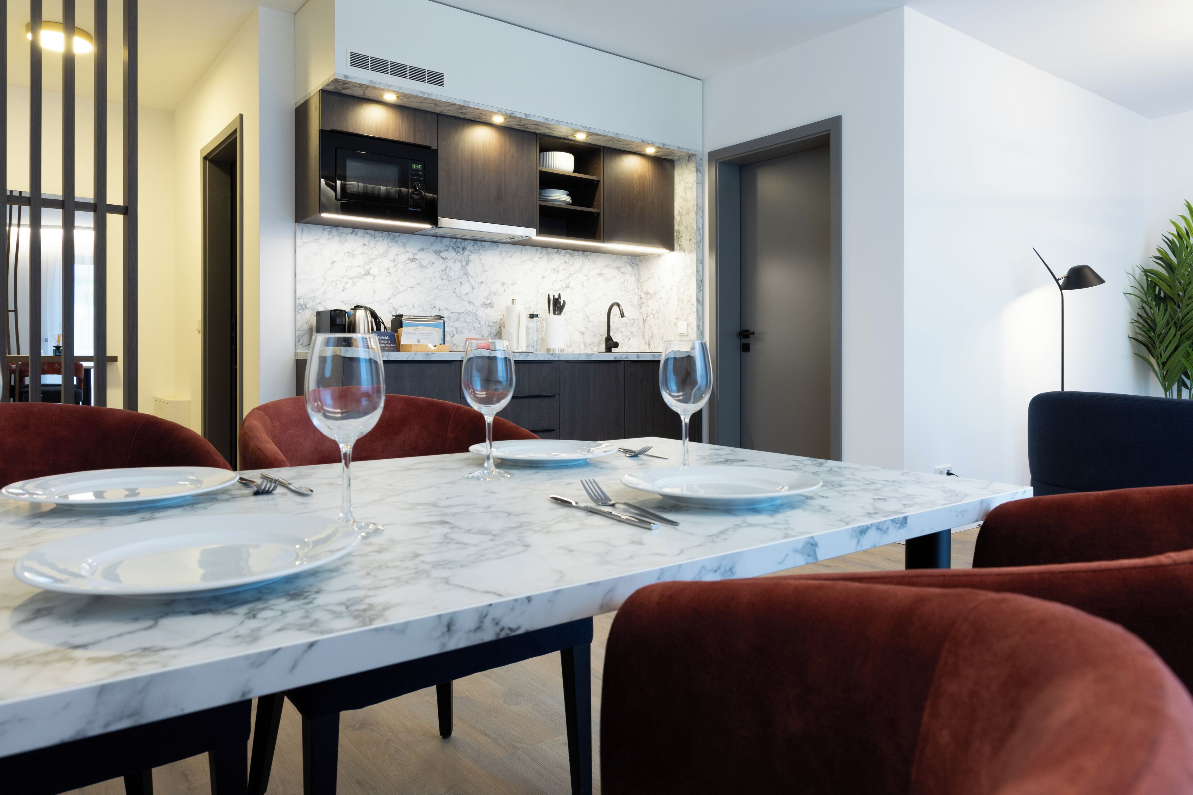 A dining area with a marble table, red chairs, and a kitchen in the background.