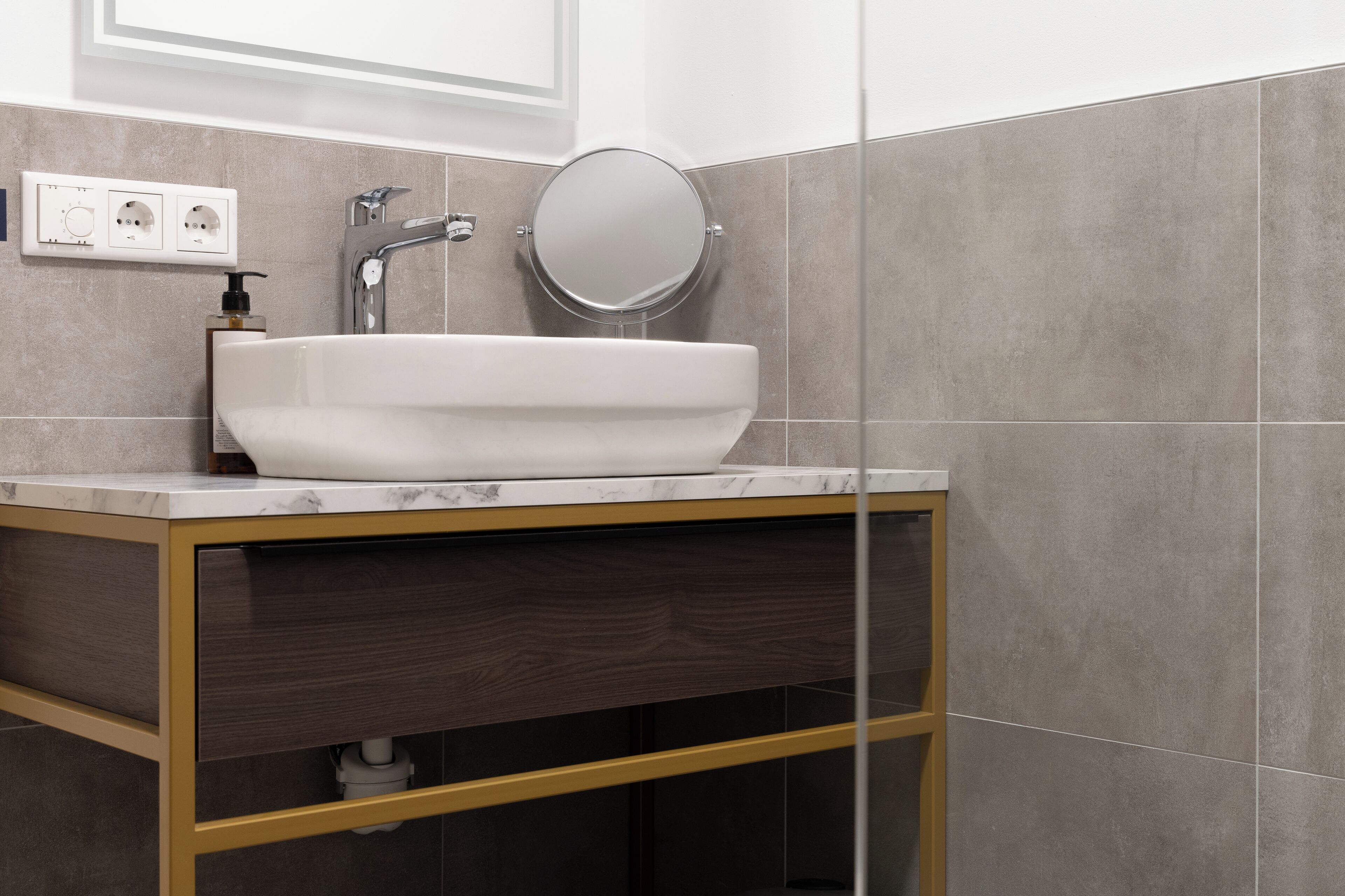A modern bathroom with a white sink, a round mirror, and a wooden vanity.