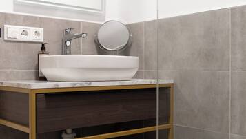 A modern bathroom with a white sink, a round mirror, and a wooden vanity.