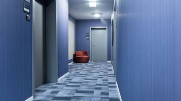 Un couloir aux murs bleus, avec un tapis à motifs et une chaise rouge.