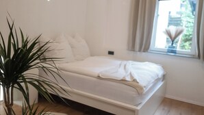 A modern bedroom with a bed, a potted plant, and a window with curtains. - DLG-STAYS - "Pure 23" (Iserlohn)