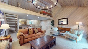 A spacious living area with a brown leather sofa, a wooden coffee table, and a light blue armchair. A dining table with chairs is visible in the background.