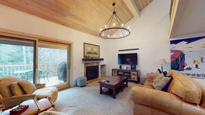 A living room with a fireplace, a television, and a large window overlooking a deck.