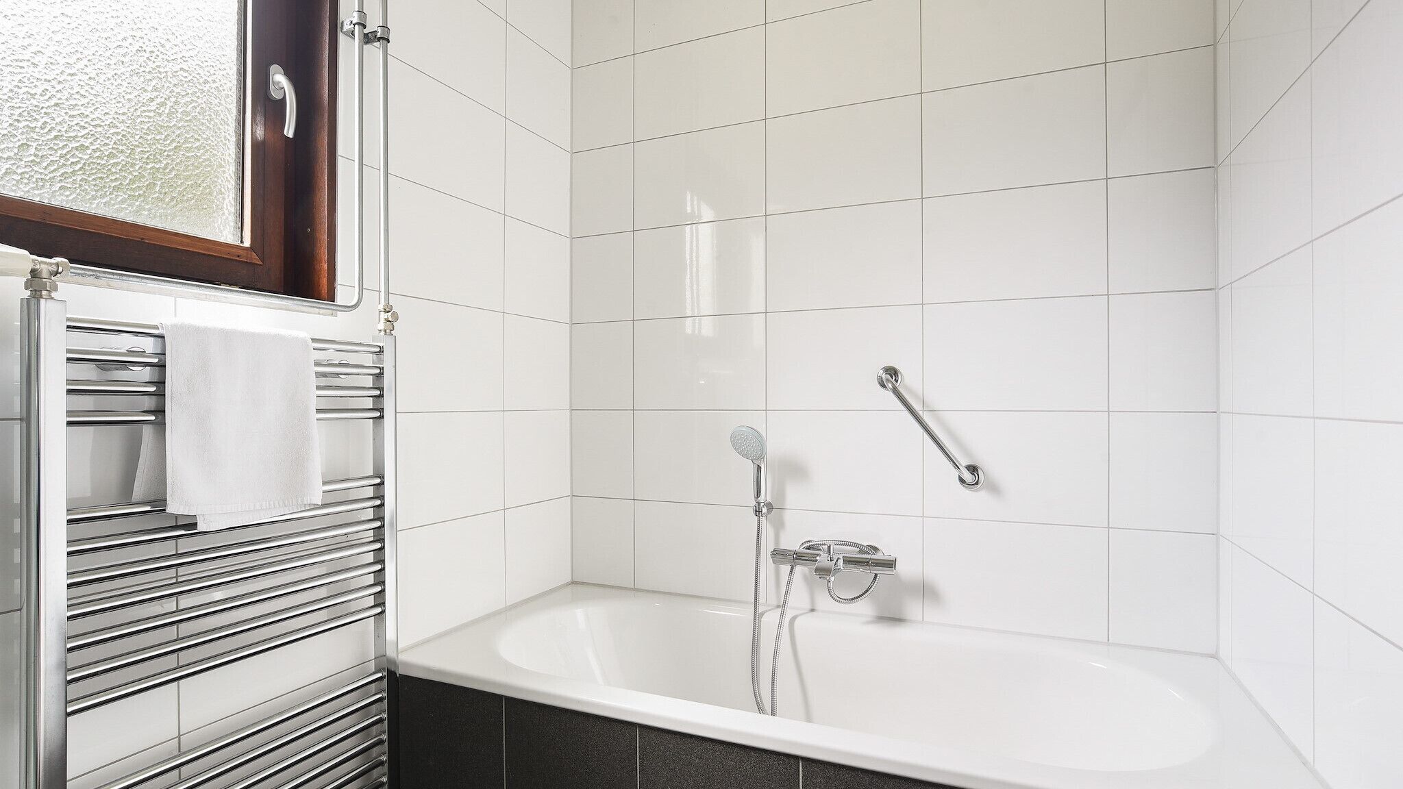 A modern bathroom with a white bathtub, a glass shower enclosure, and a towel rack with a white towel.