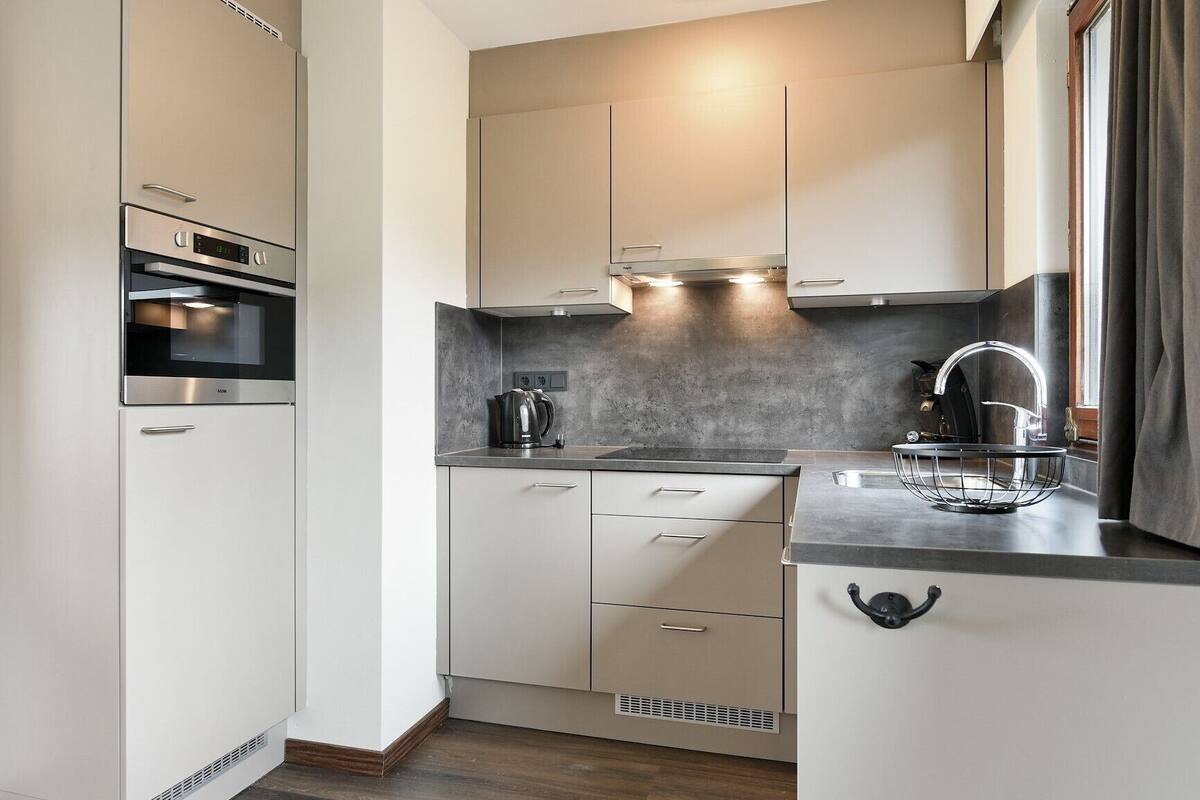 A modern kitchen with a built-in oven, a kettle, and a sink with a faucet.