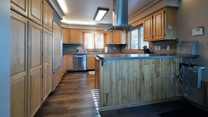 Eine moderne Küche mit Holzschränken, einer zentralen Kochinsel, Edelstahlgeräten und einer eingebauten Dunstabzugshaube.