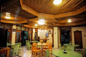 Un restaurante con vigas de madera en el techo, sillas verdes y mesas redondas.