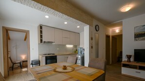 Une cuisine moderne avec des meubles blancs, une cuisinière et un distributeur d’eau. On y trouve un coin repas avec une table et des chaises en bois, ainsi qu’un salon avec un téléviseur et un canapé.
