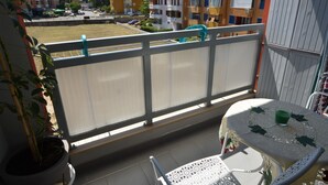 Un balcón con una mesa y sillas, una planta en maceta y vistas de edificios de varios pisos.