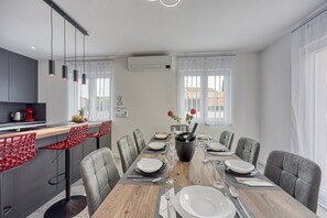 A modern dining area with a wooden table set for six, grey upholstered chairs, and a kitchen counter with red chairs. - Peaceful Blooming Villa With Pool (Rovinj)