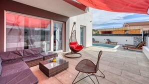 A modern outdoor patio with a sofa, a wicker table, a hanging chair, and a pool in the background. - Peaceful Blooming Villa With Pool (Rovinj)