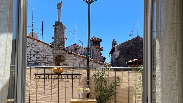 A balcony with wicker furniture, a potted plant, and a table with a glass of wine. - Enchanting Quiet Residence Rovinj Downtown (Rovinj)