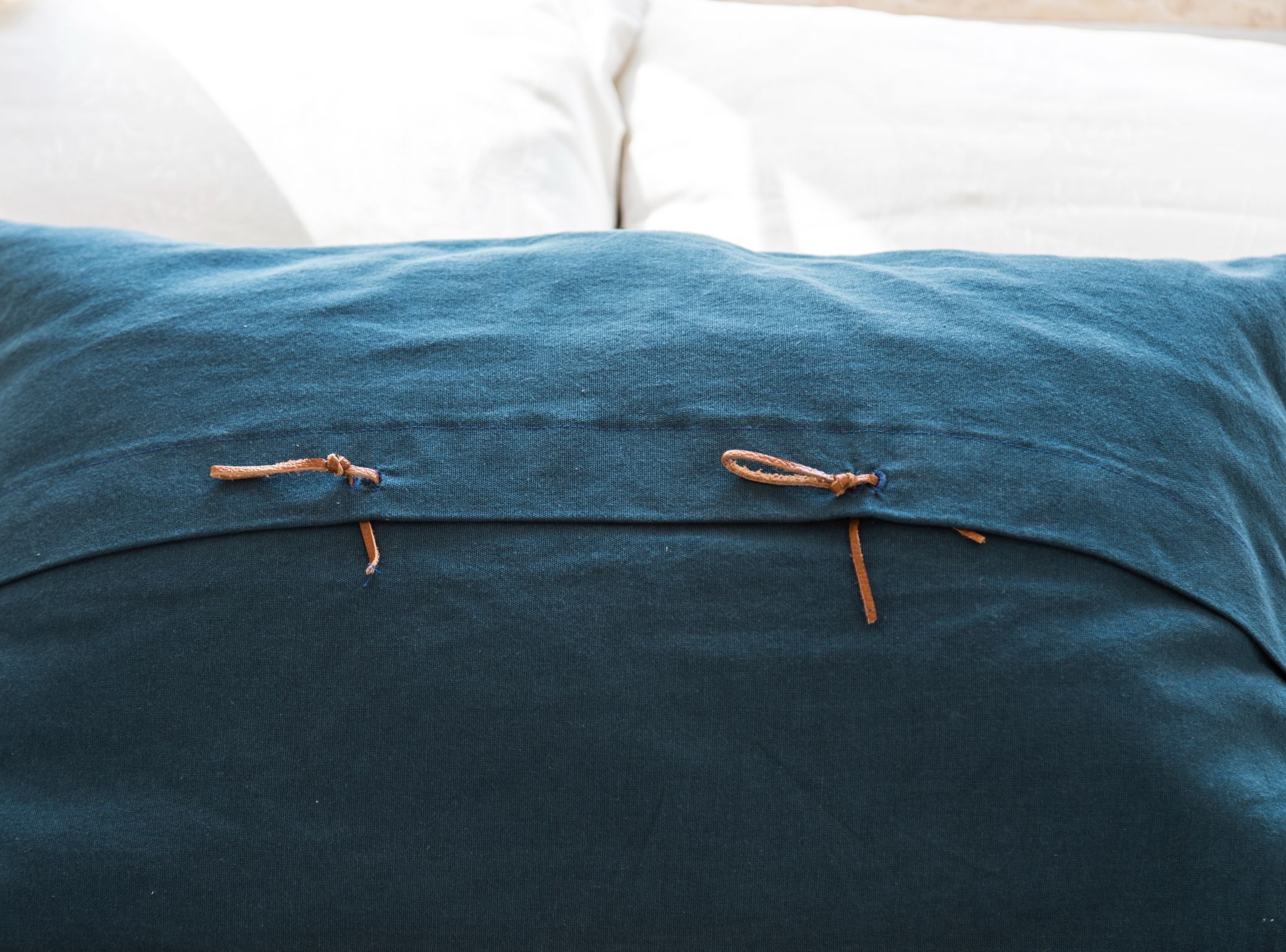 A blue pillow with two brown tassels on a white bed.