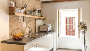 Une cuisine avec un mur en briques, des poutres en bois, un réfrigérateur blanc, un grille-pain et un panier de fruits.