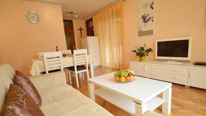 Uma sala de estar com sofá, mesa de jantar com cadeiras, televisão e uma fruteira.