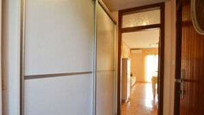 Corredor com porta deslizante que dá para um quarto com geladeira e cama.