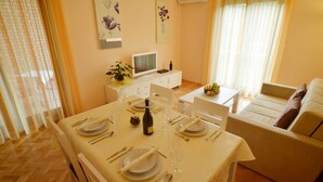 Uma sala bem iluminada com uma área de jantar com mesa posta para quatro, televisão e sofá.