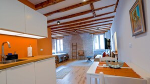 A compact kitchen with a wooden ceiling, a dining area with a table and chairs, and a stone wall. - Alluring Studio Apartment Downtown Rovinj (Rovinj)