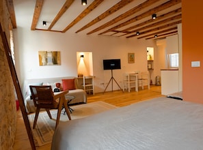 A cozy room with a wooden ceiling, a television on a tripod, a sofa, a small table, and a kitchen area in the background. - Alluring Studio Apartment Downtown Rovinj (Rovinj)