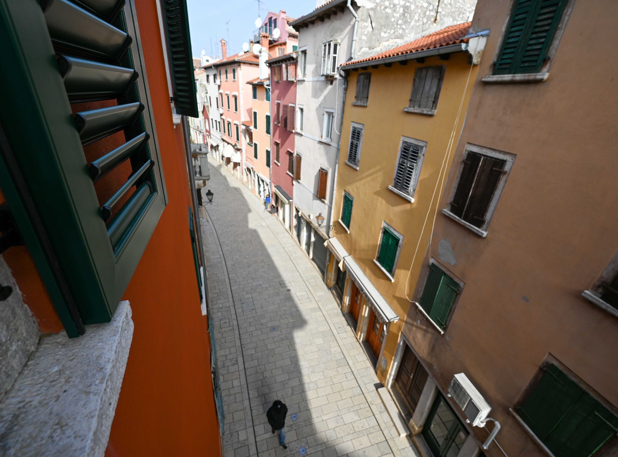 A narrow street with colorful buildings, a person walking, and a clear sky.