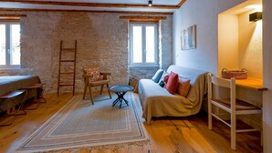 A cozy room with exposed wooden beams, a stone wall, a sofa with cushions, a small table, and a chair. - Alluring Studio Apartment Downtown Rovinj (Rovinj)