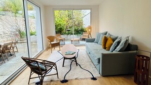 A spacious living room with a grey sofa, wooden flooring, and a large window offering a view of greenery. - Charming seaside house (Concarneau)