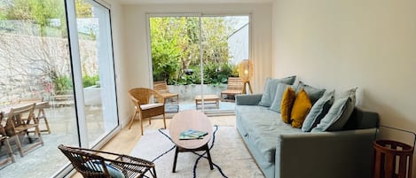 Amplia sala de estar con un sofá gris, piso de madera y un ventanal con vistas a la vegetación.