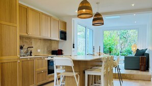 A modern kitchen with wooden cabinets, a white dining area, and a large window offering a view of greenery. - Charming seaside house (Concarneau)