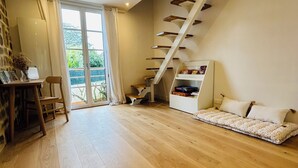 A spacious room with a wooden floor, a white sofa, a staircase, and a bookshelf. - Charming seaside house (Concarneau)