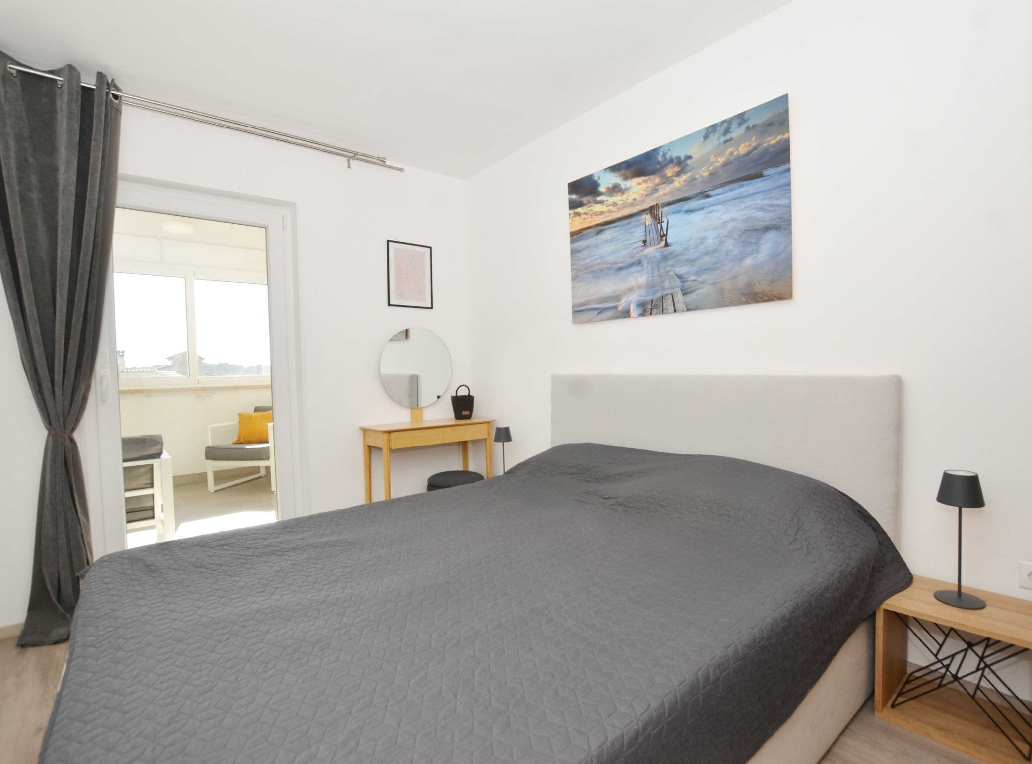 Ein Schlafzimmer mit einem großen Bett, einem Schreibtisch mit Spiegel, einem kleinen Tisch und einem Gemälde an der Wand.