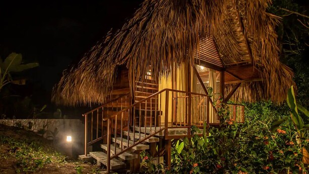 A thatched-roof building with a wooden staircase leading to a porch. - Cozy Cabin Nestled in Bamboo Forest (El Caimo)