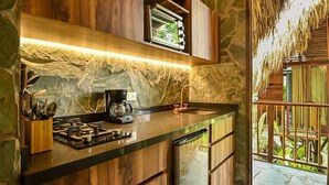 A kitchen with a stone backsplash, wooden cabinets, and a built-in dishwasher. - Cozy Cabin Nestled in Bamboo Forest (El Caimo)