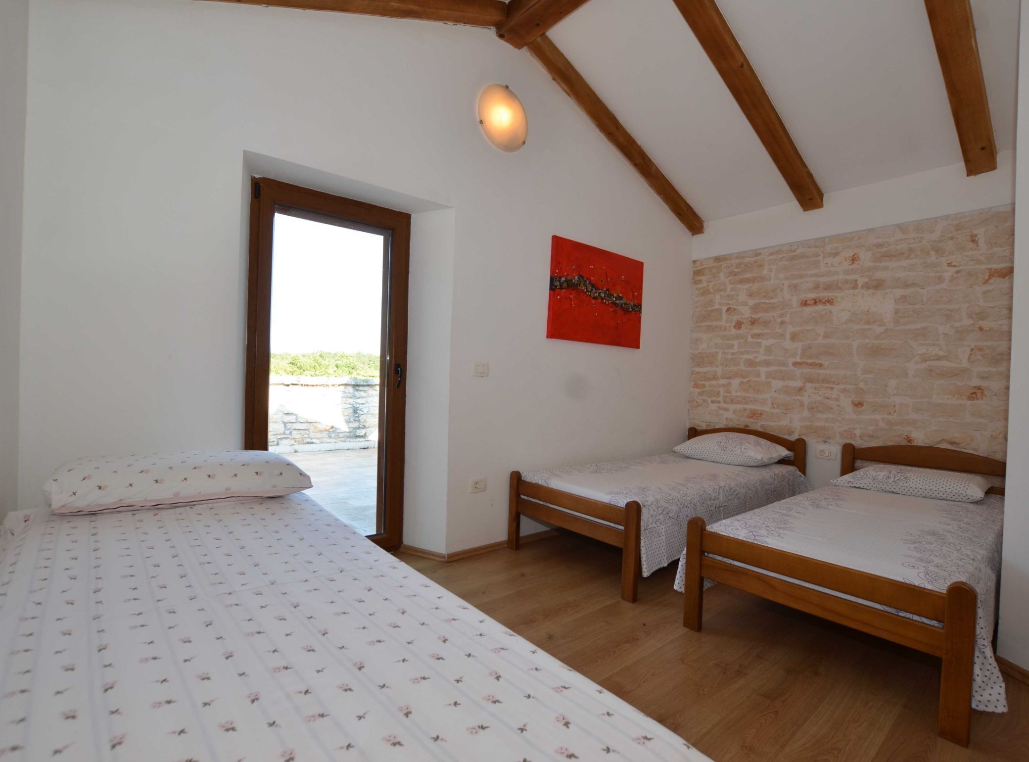 A bedroom with two wooden beds, a large bed, a red abstract painting, and a stone wall.