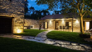 A stone building with a paved driveway leading to a covered patio area with outdoor seating.