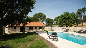 A stone building with a tiled roof, a swimming pool, and outdoor seating.