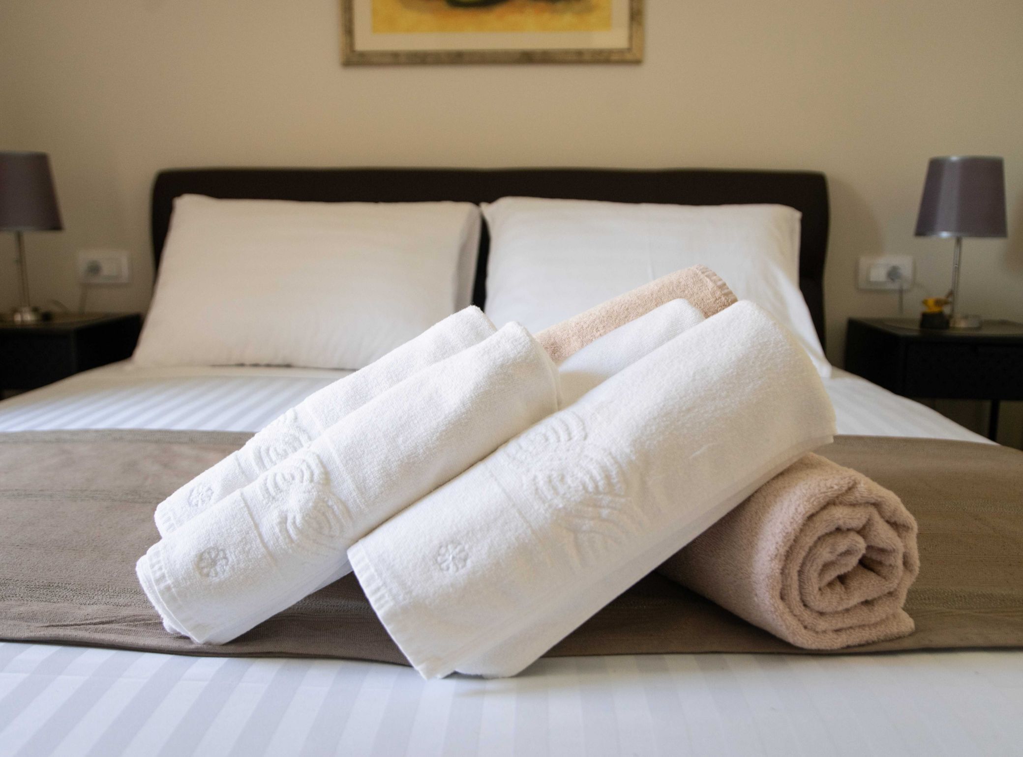 A neatly made bed with white and beige towels, a brown bedspread, and a framed picture on the wall.