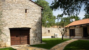 A stone building with a large wooden door, a stone pathway, and a small tree in the yard.