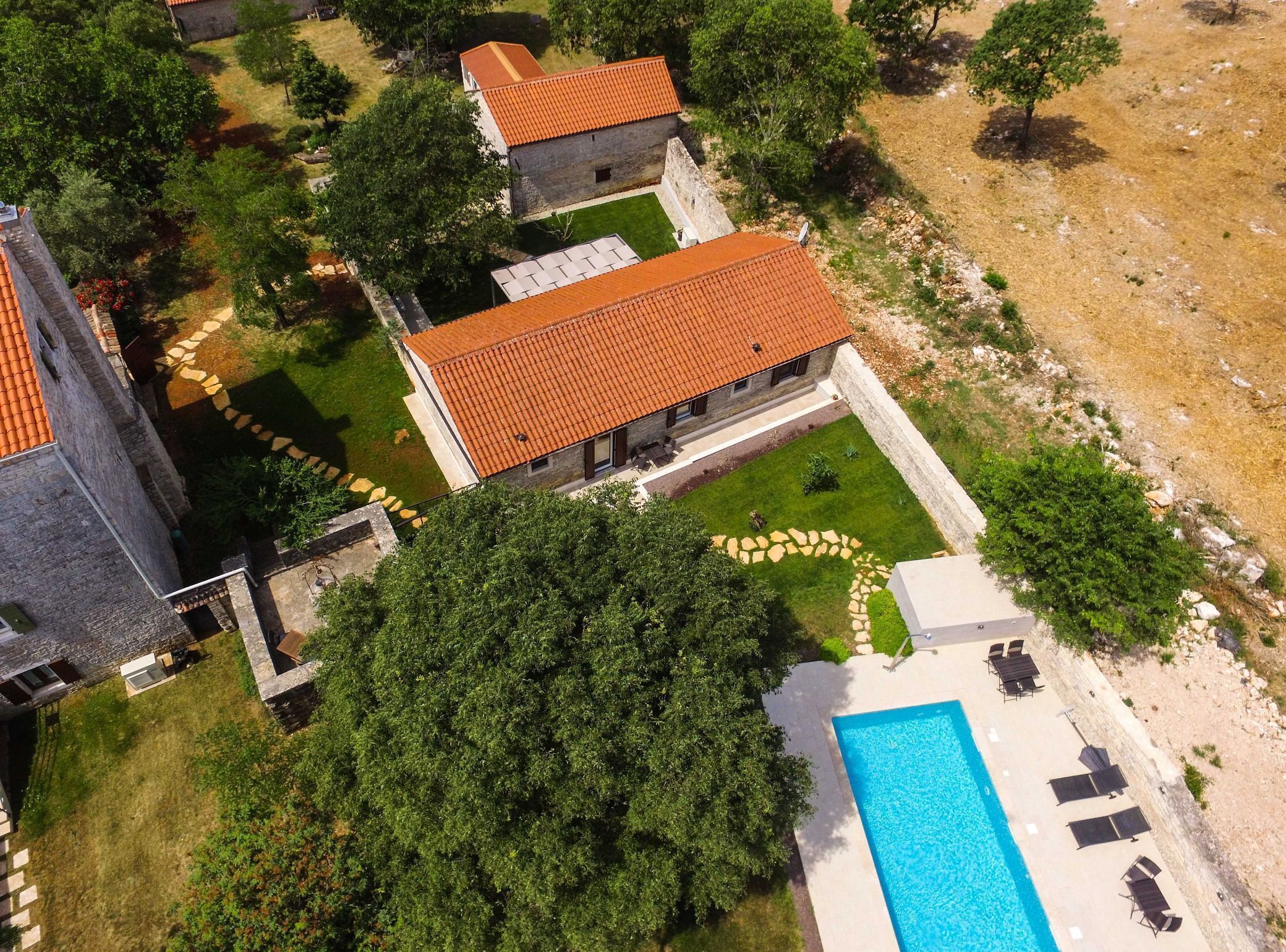 An aerial view of a property with a swimming pool, stone pathway, and a building with a tiled roof.