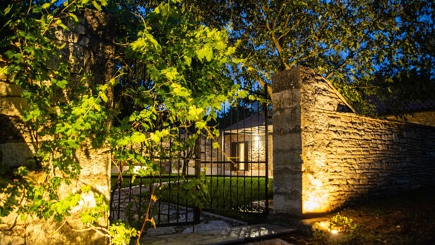 A stone wall with a metal gate, a stone pathway, and a building in the background.