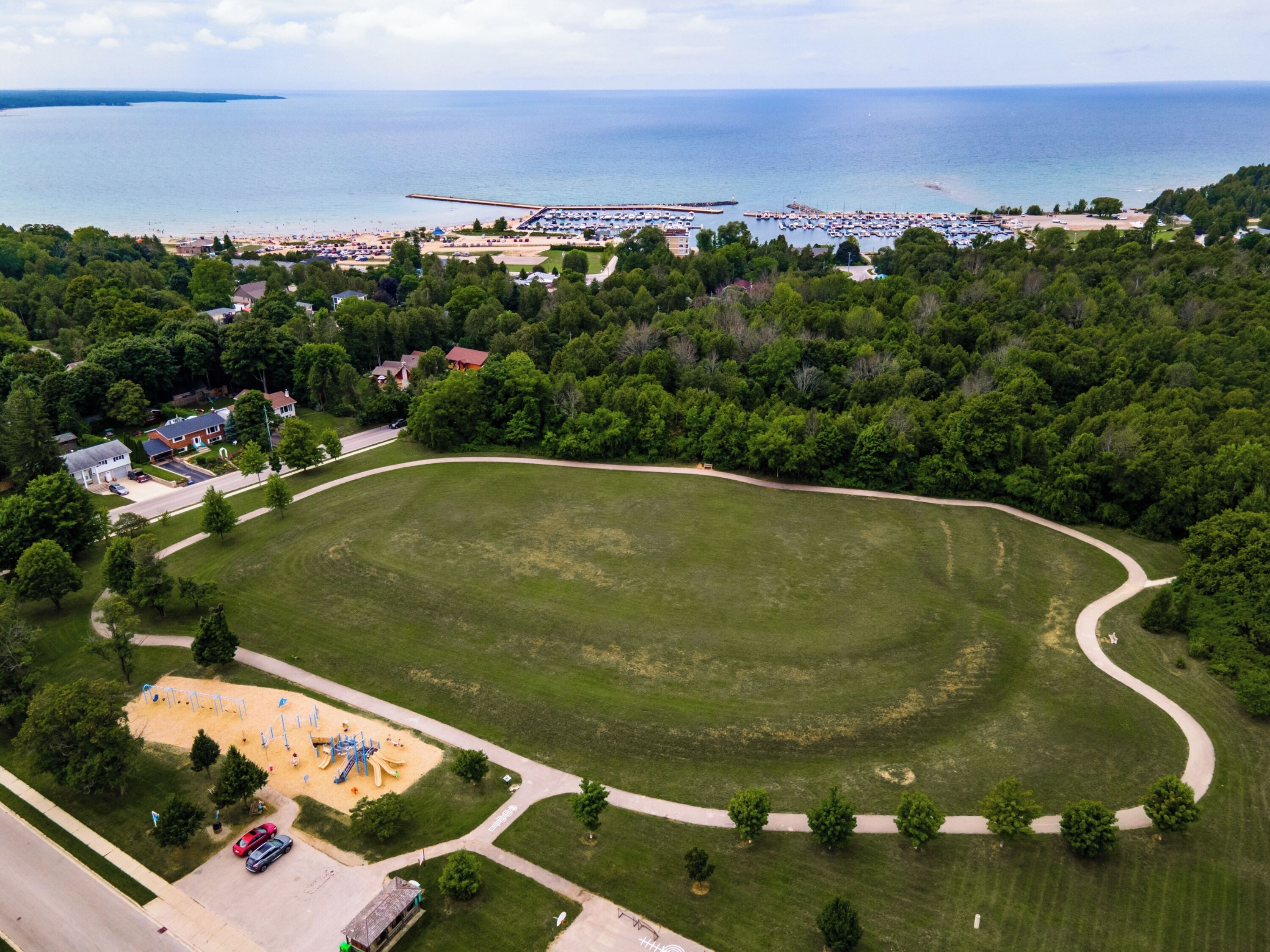 An aerial view of a park with a playground, a road, and a beach area with a pier.