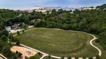 An aerial view of a park with a playground, a road, and a beach area with a pier.