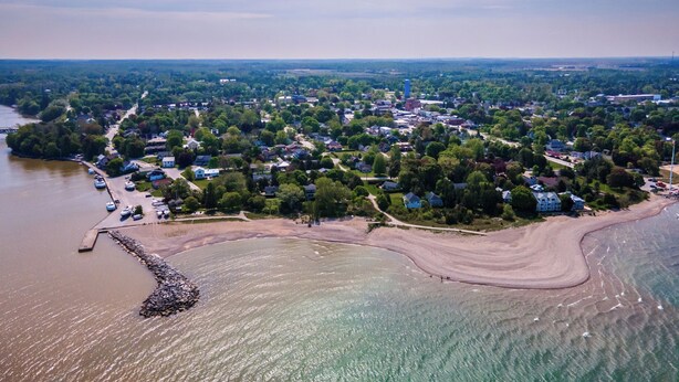 Ett flygbildsbild av en kuststad med en småbåtshamn, bostadsområden och en strand.