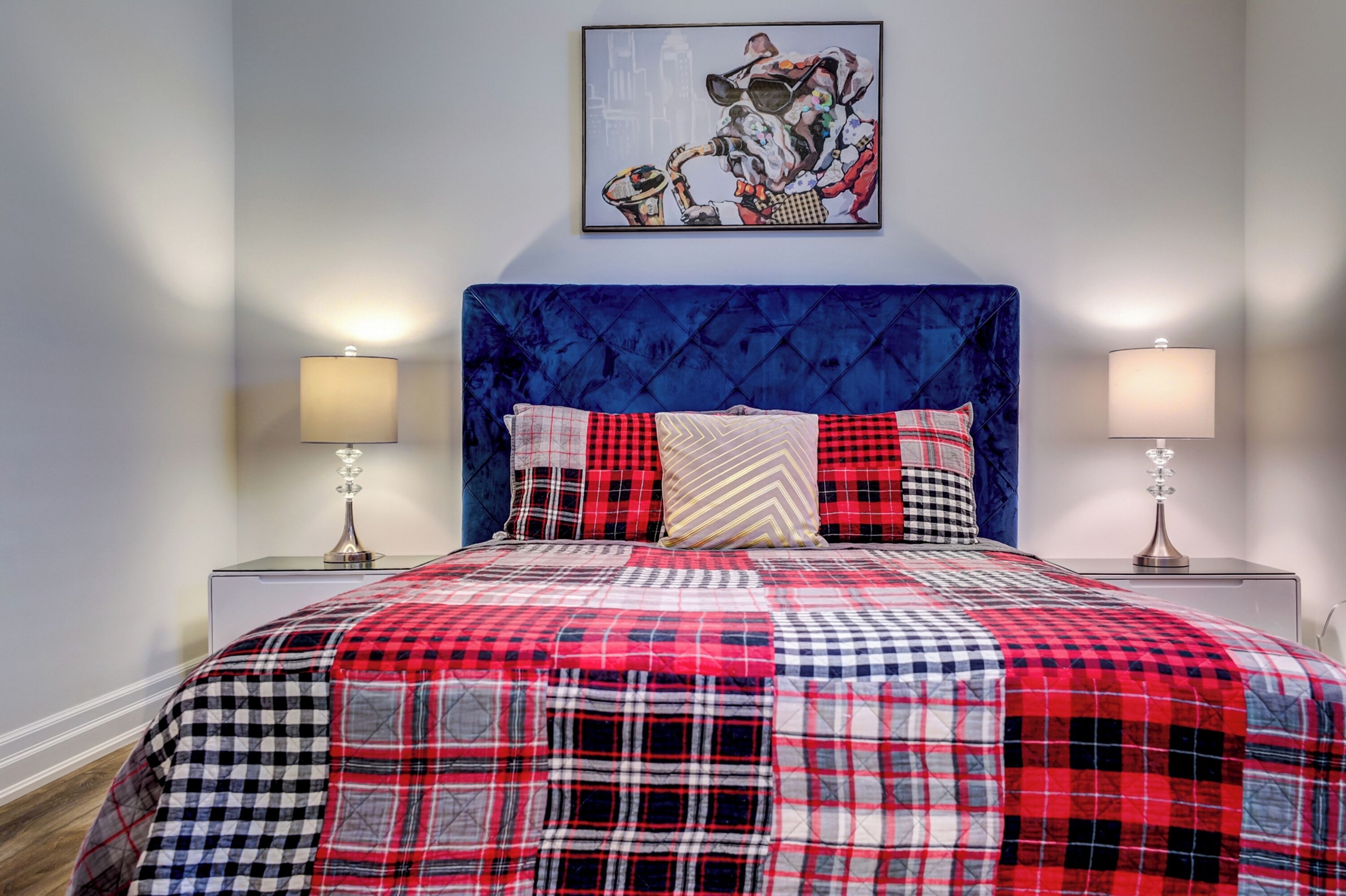 A bed with a red and black checkered quilt, a blue upholstered headboard, and two bedside lamps.