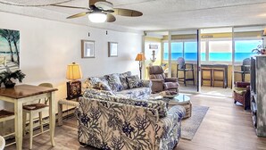 A living room with a large sofa, a dining table, and a ceiling fan. There is a view of the ocean through the sliding glass doors. - 20th Floor Ocean Front Condo! Steps to the Beach and Ocean! Atlantis #2004 (Ocean City)