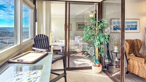 A room with a glass partition, a dining table with a cake, a chair, a potted plant, and a view of the sea through the window. - 20th Floor Ocean Front Condo! Steps to the Beach and Ocean! Atlantis #2004 (Ocean City)