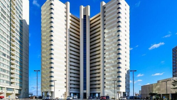 A high-rise building with a central elevator shaft, surrounded by parking spaces and other buildings. - 20th Floor Ocean Front Condo! Steps to the Beach and Ocean! Atlantis #2004 (Ocean City)