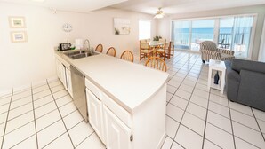 A modern kitchen with a central island, dining area with chairs, a gray sofa, and a view of the ocean through large windows.
